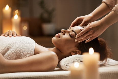 Woman receiving facial massage with lit candles in background
